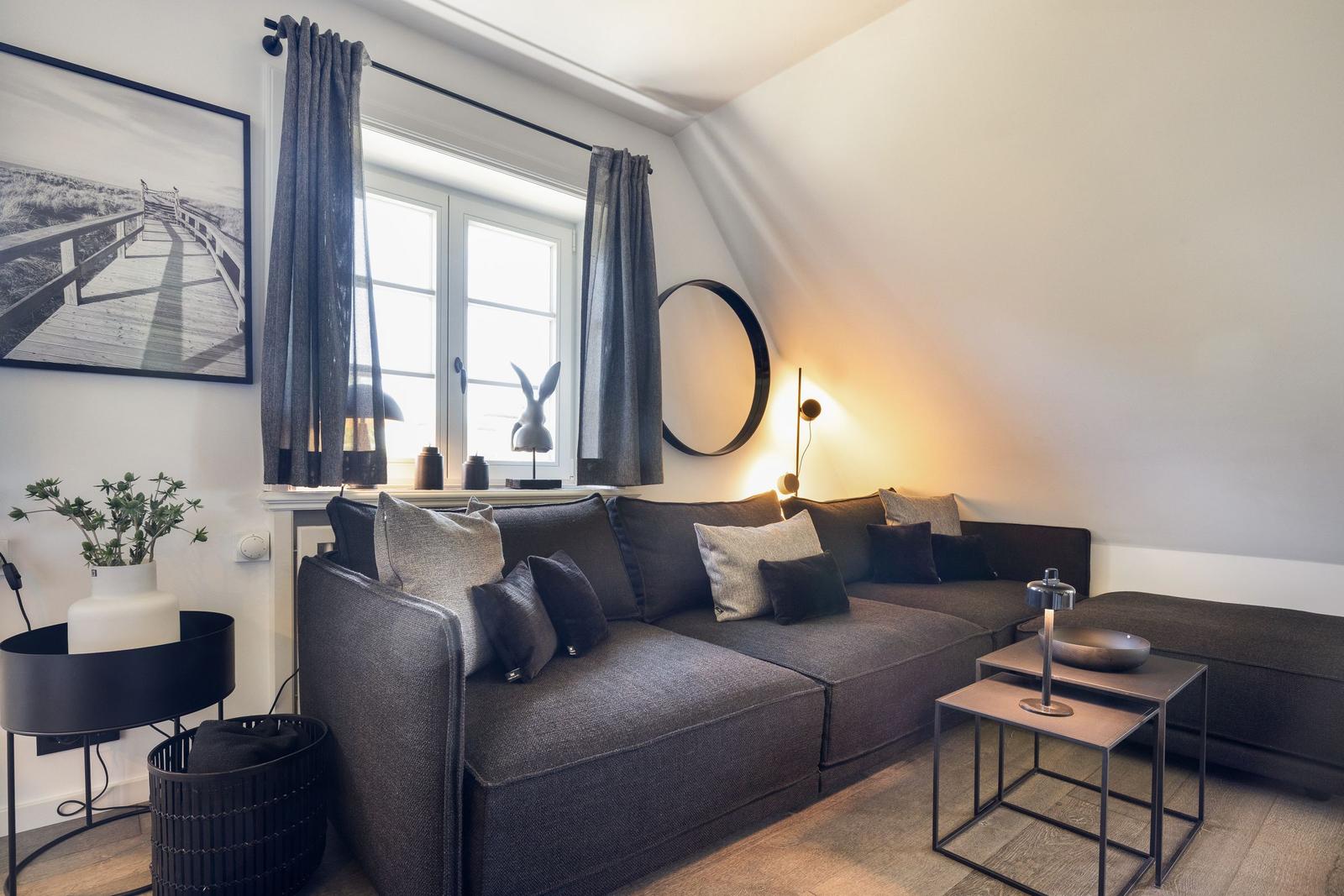 Ein Wohnzimmer mit grauem Sofa, Fenster und modernen Möbeln.