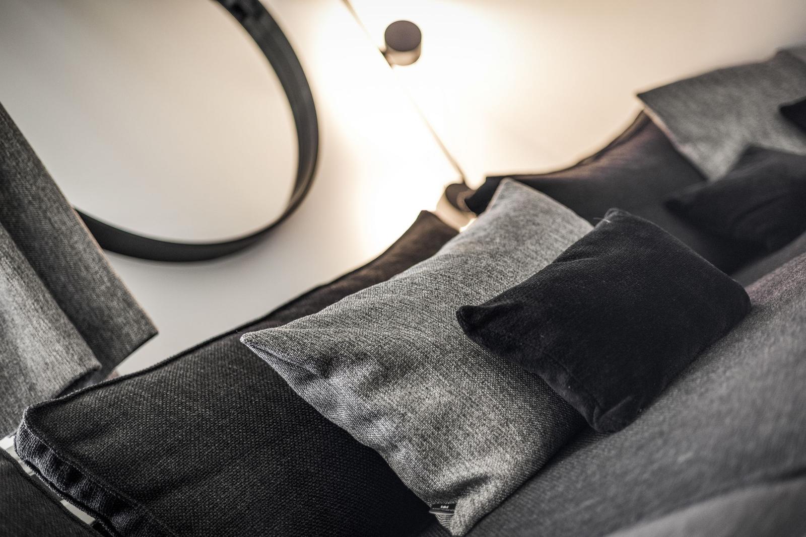 Schwarze und graue Kissen auf einem Sofa mit runden Wandspiegel und Beleuchtung.