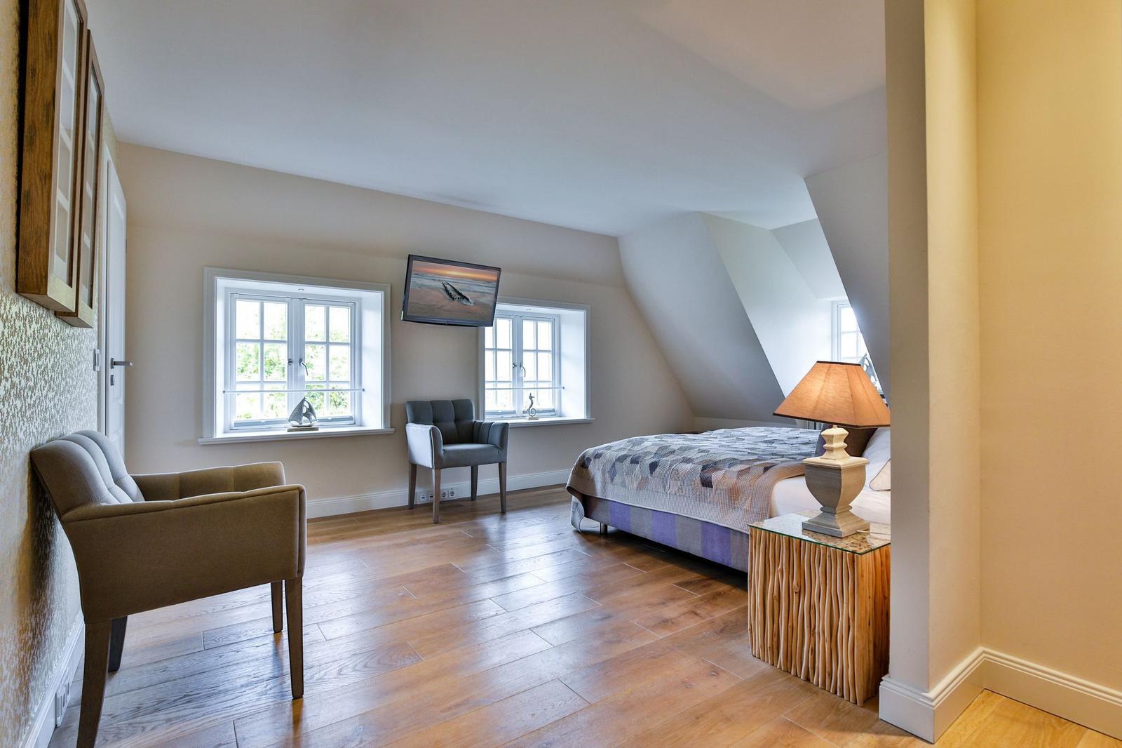 Schlafzimmer mit Bett, Fenstern, TV und Holzboden.
