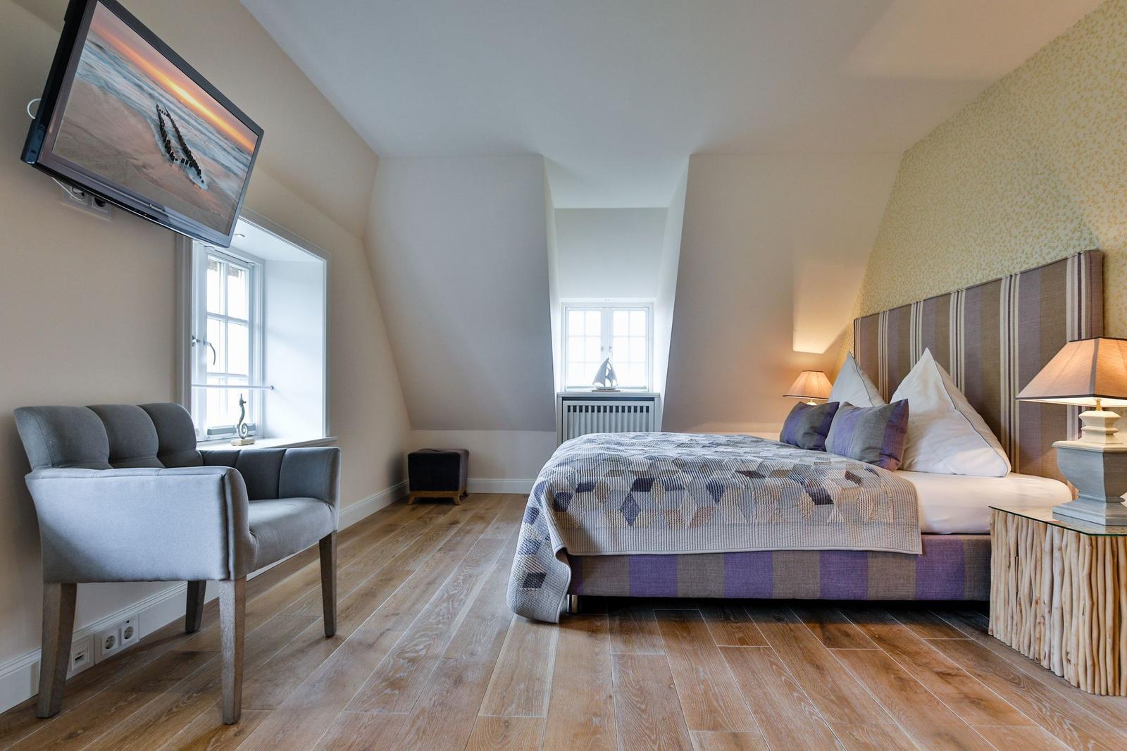 Schlafzimmer mit Bett, TV und Holzboden.