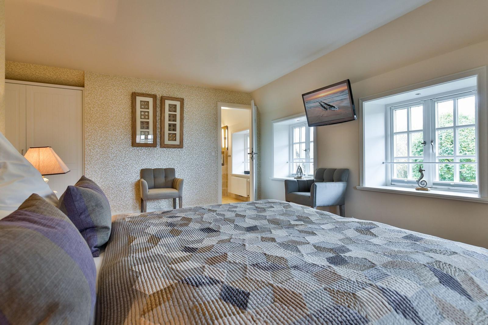 Schlafzimmer mit Bett, Fenstern und Fernseher an der Wand.