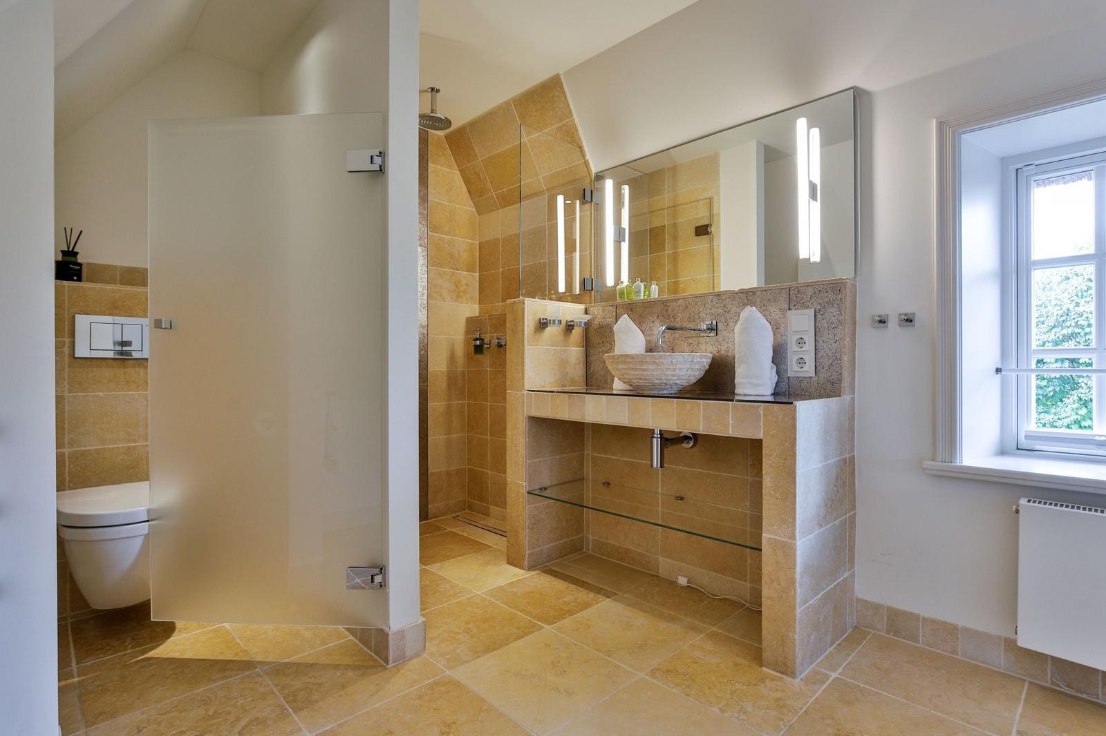 Badezimmer mit Dusche, Waschbecken und Toilette. Holzfliesen und Spiegel.