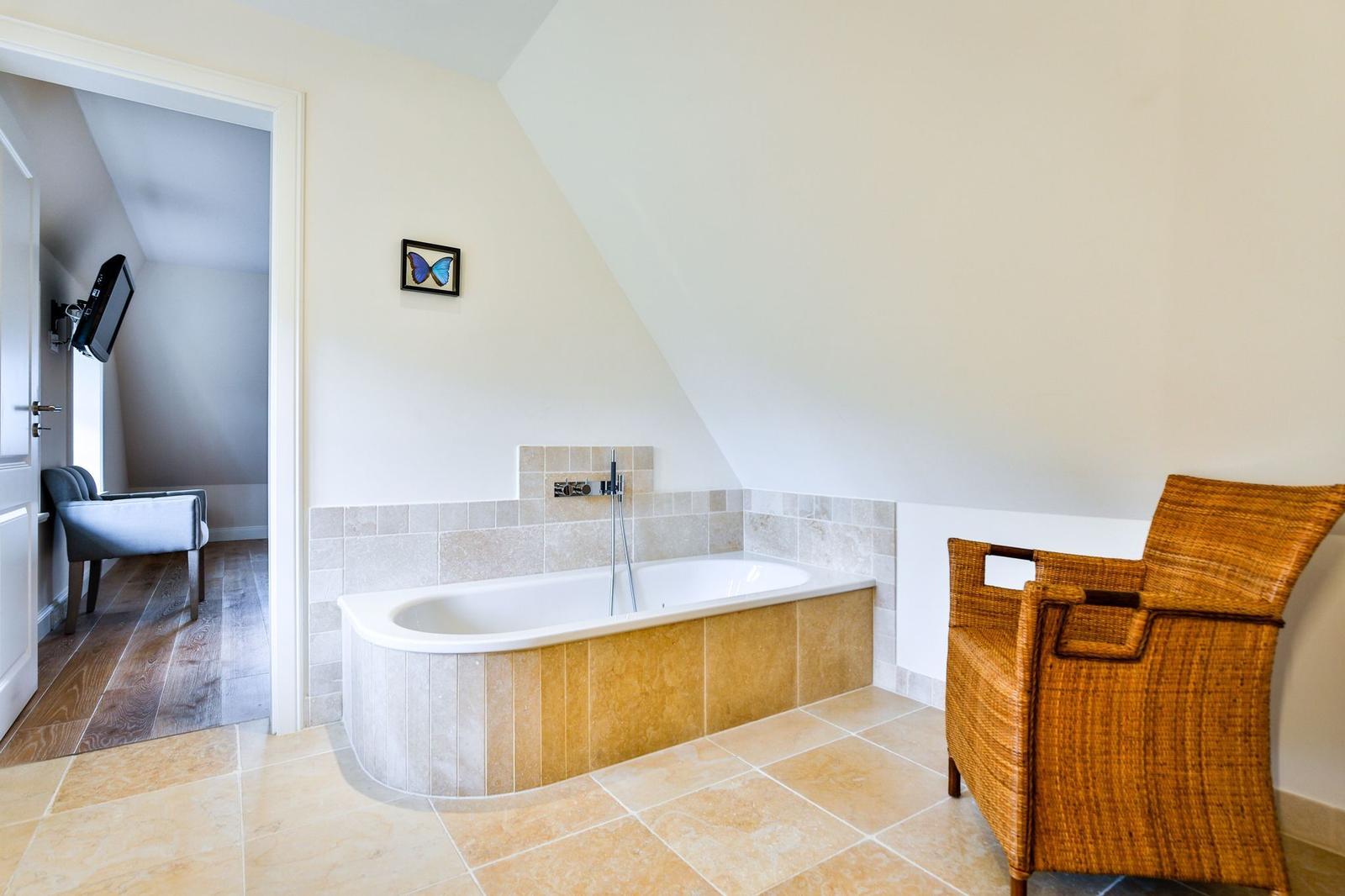 Bad mit Badewanne, Wickerstuhl und Blick in Schlafzimmer