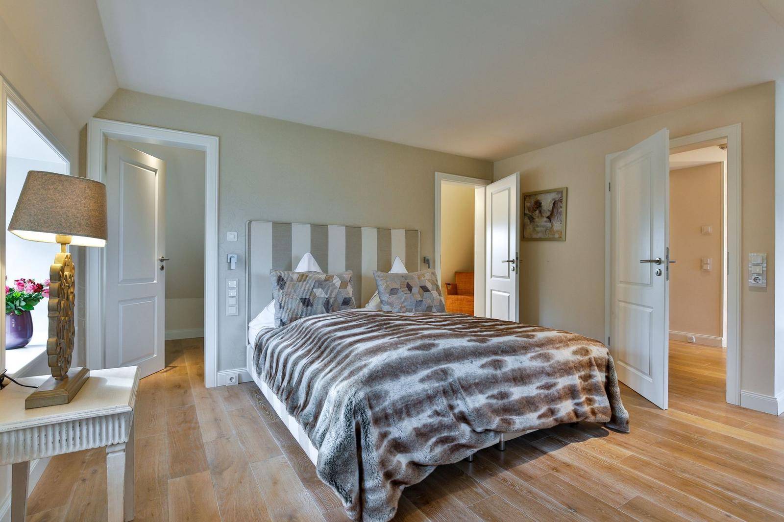 Schlafzimmer mit Bett, Holzboden und Türen zu angrenzenden Räumen.