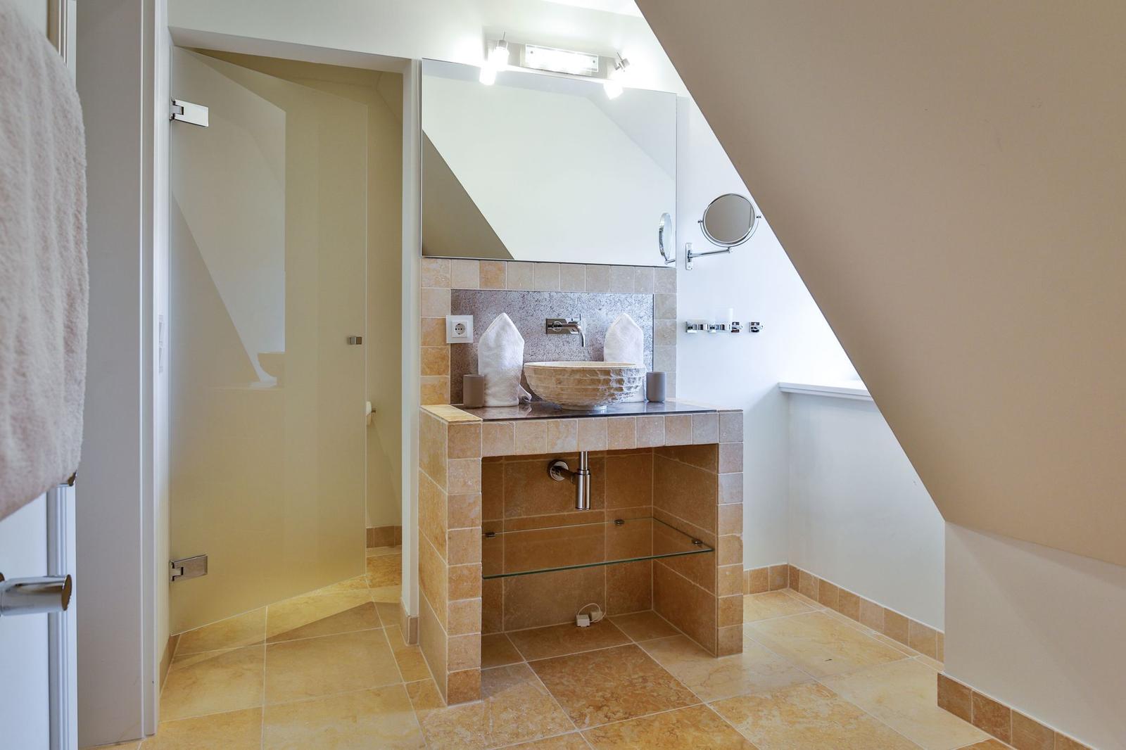 Badezimmer mit Steinwaschbecken, Spiegel und Dusche unter Dachschrägen.