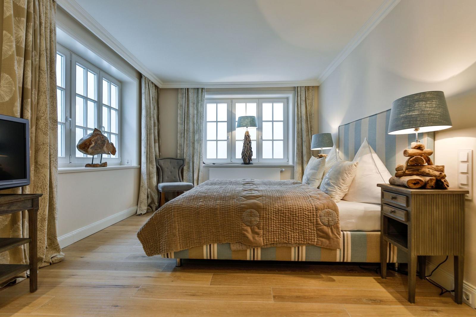 Schlafzimmer mit Bett, zwei Fenstern und Holzboden.