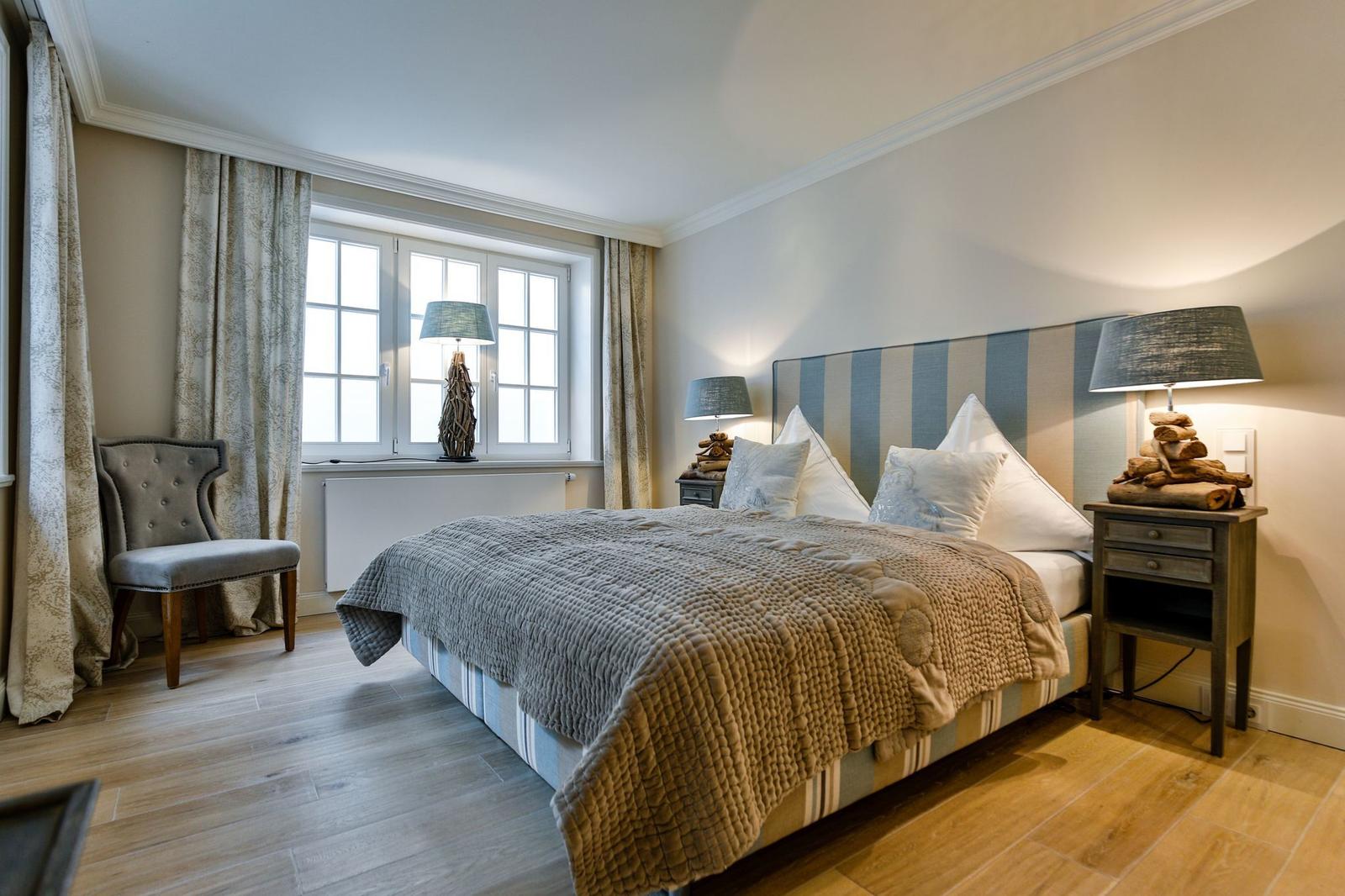 Schlafzimmer mit Bett, Nachttischen und Fenster mit Vorhängen.