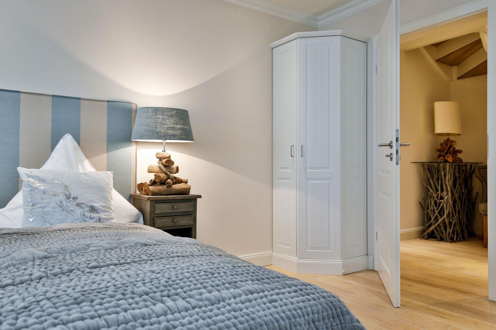 Schlafzimmer mit Bett, Nachttisch und Kleiderschrank. Tür führt in angrenzendes Zimmer.