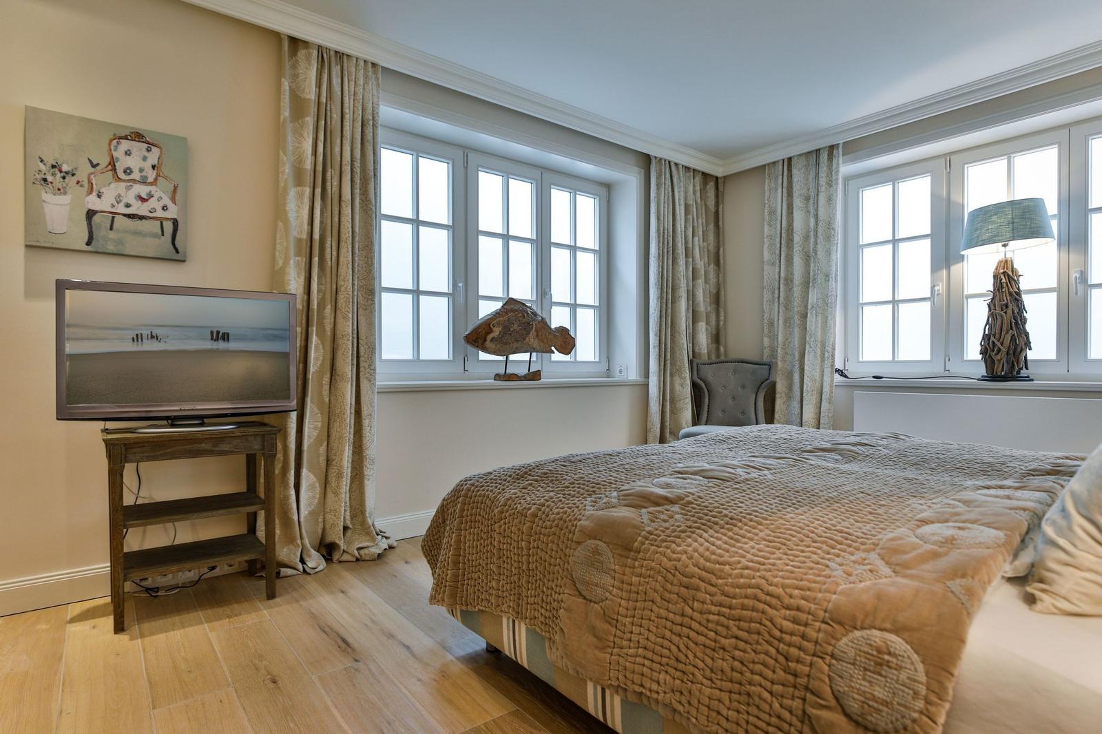 Schlafzimmer mit Bett, TV und Fenstern mit Vorhängen.
