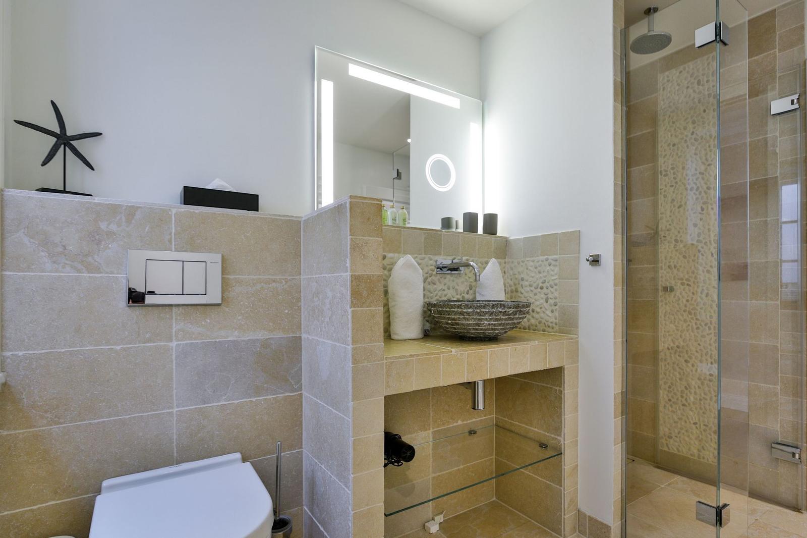 Badezimmer mit Dusche, Waschbecken und Toilette. Steinwand und Spiegel.