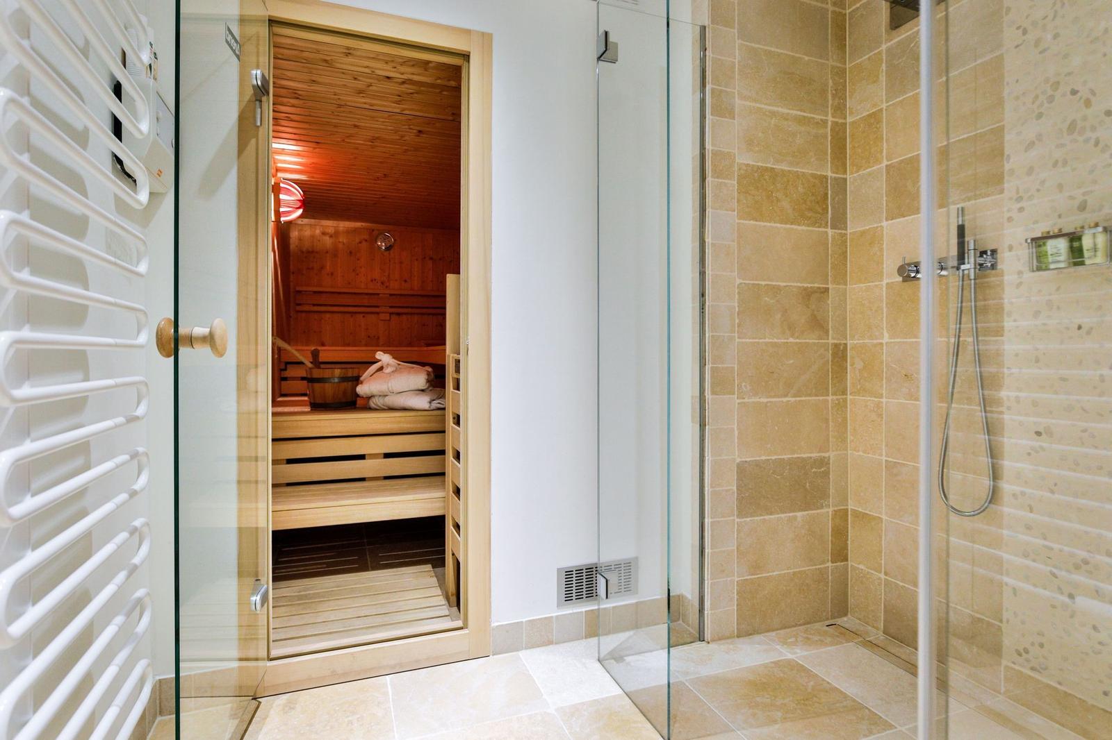 Dusche mit Glaswand und Sauna mit Holzbänken und Handtuch.