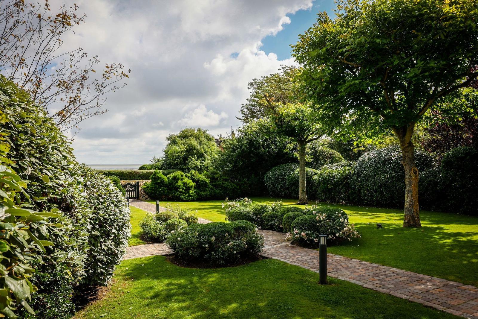 Gartenweg mit Rasen, Sträuchern und Bäumen führt zum Meer.