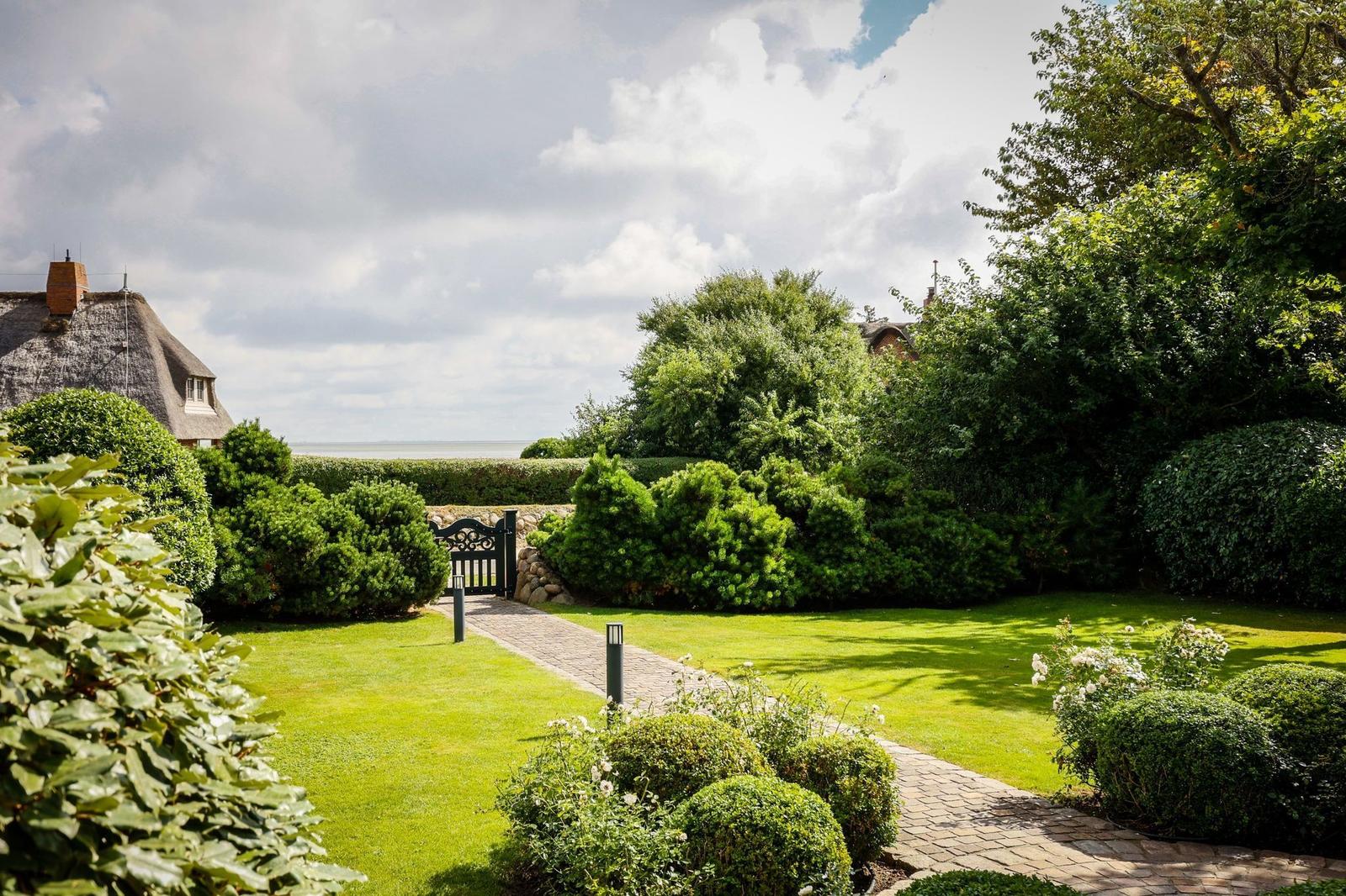 Garten mit gepflastertem Weg, grüner Rasen und Hecken. Hinterhof mit Blick auf Meer.