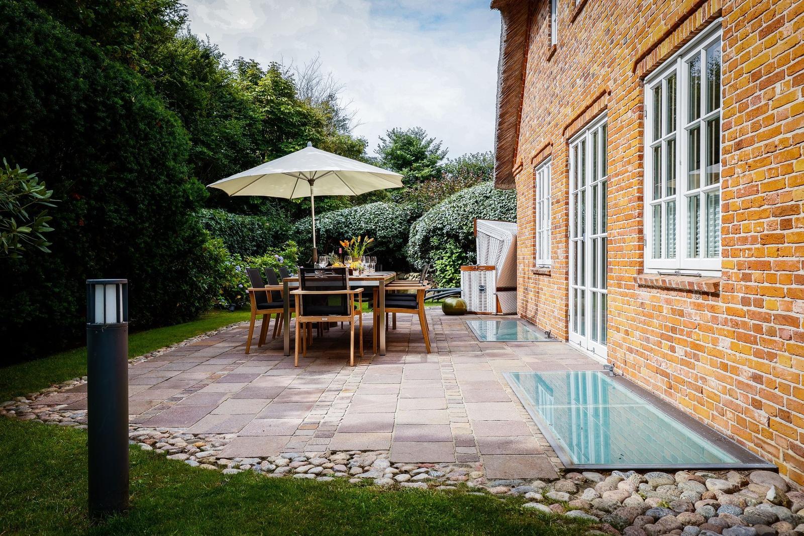 Terrasse mit Tisch, Stühlen und Sonnenschirm neben einem Haus mit Backsteinfassade.