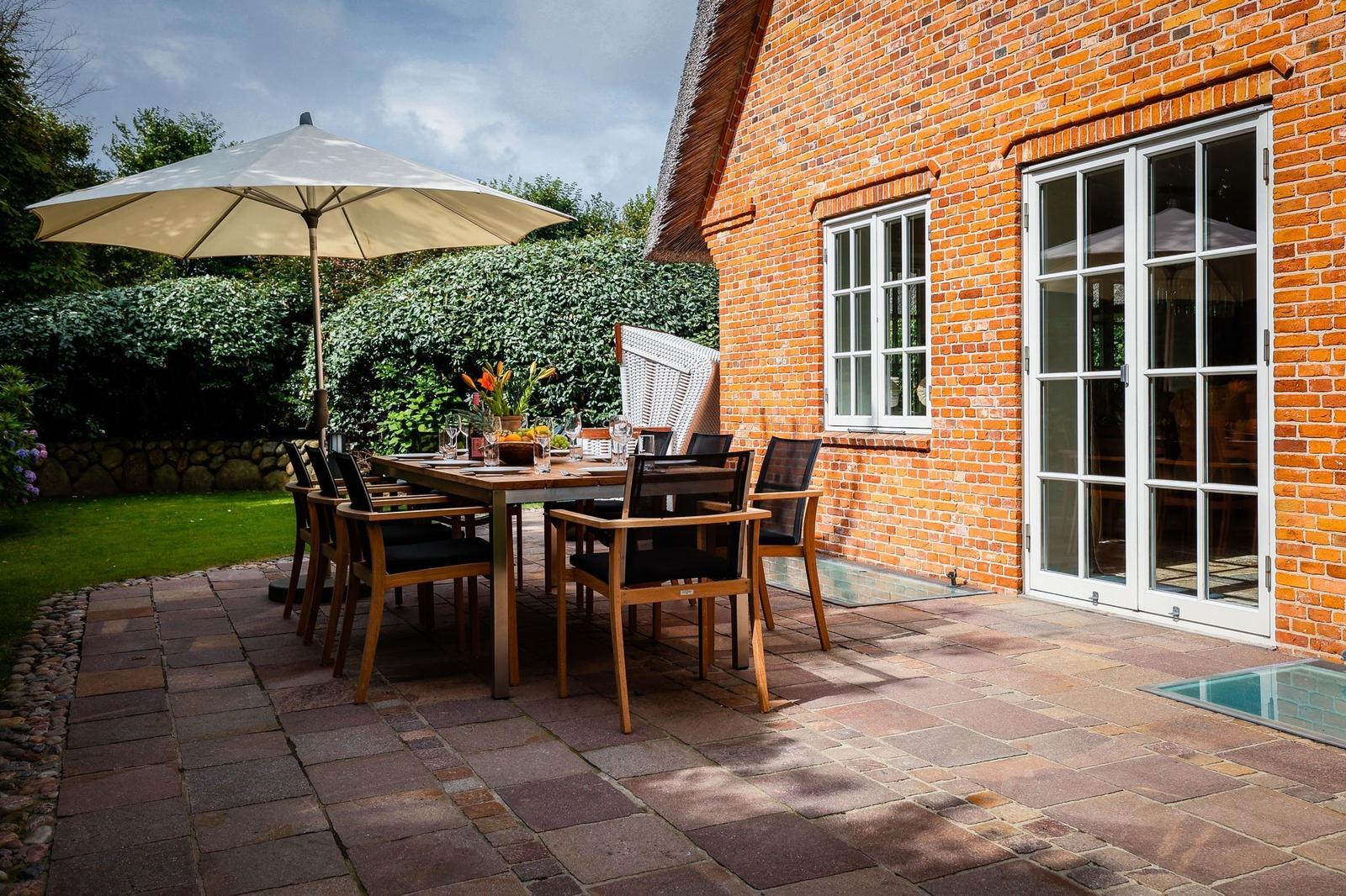 Terrasse mit Tisch, Stühlen und Sonnenschirm neben Backsteinhaus