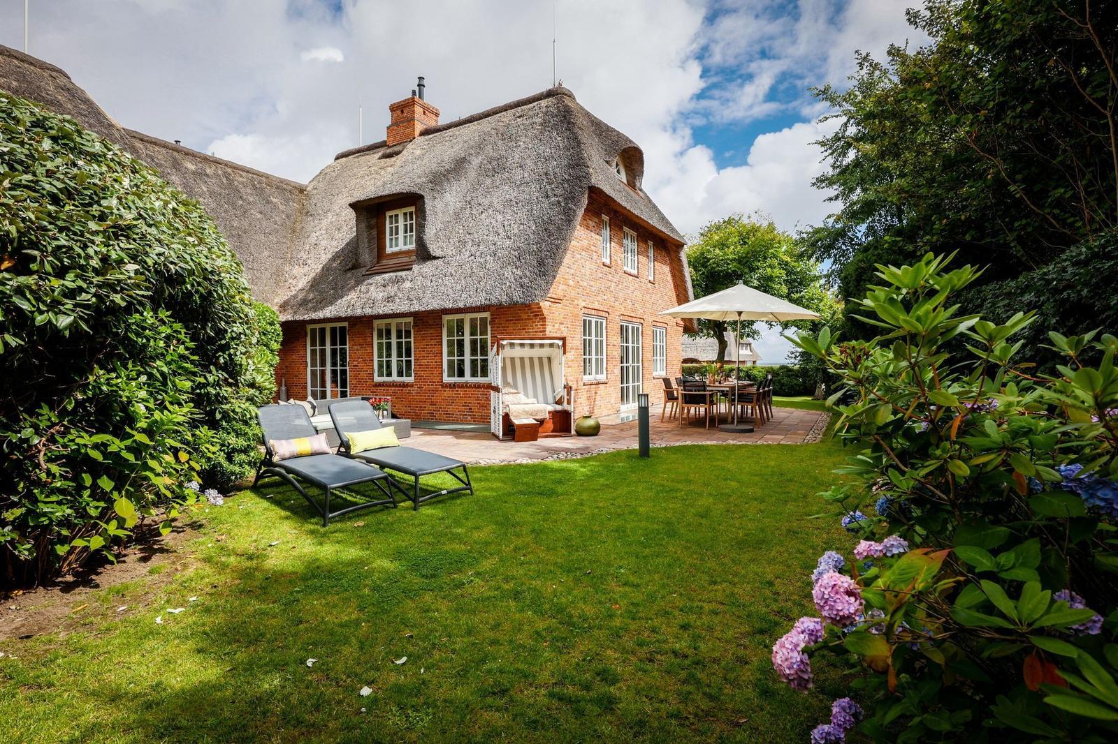 Haus mit Strohdach, Garten mit Liegestühlen und Terrasse mit Tisch.