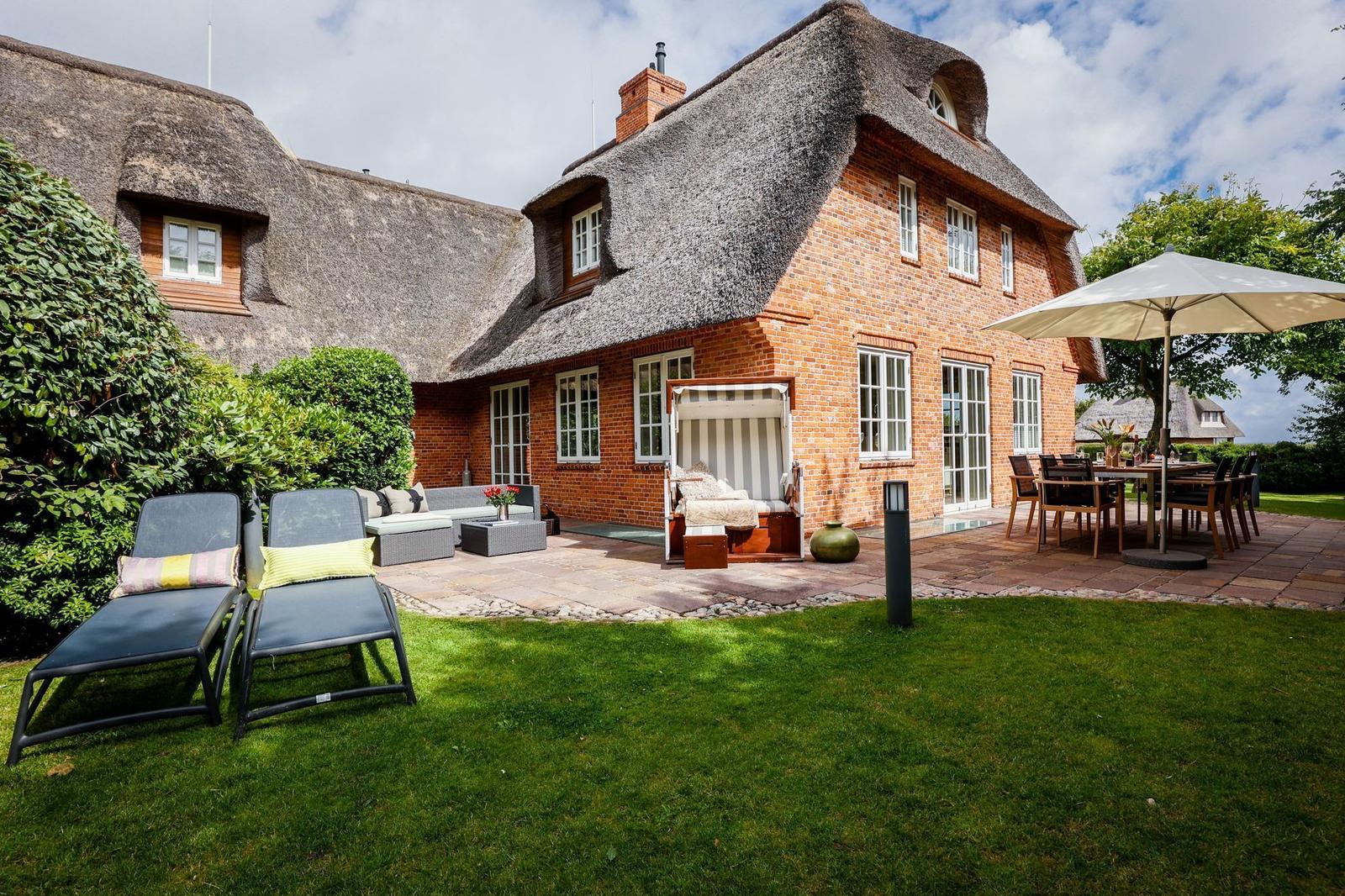 Haus mit Strohdach, Terrasse, Liegestühle und Garten.