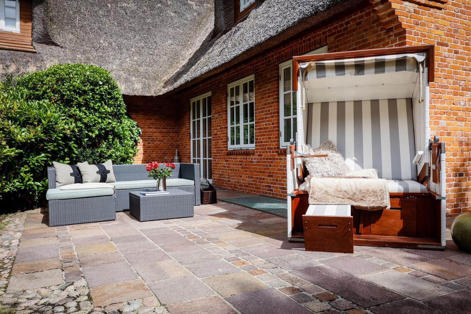 Terrasse mit Loungemöbeln und Strandkorb an Backsteinhaus mit Strohdach.