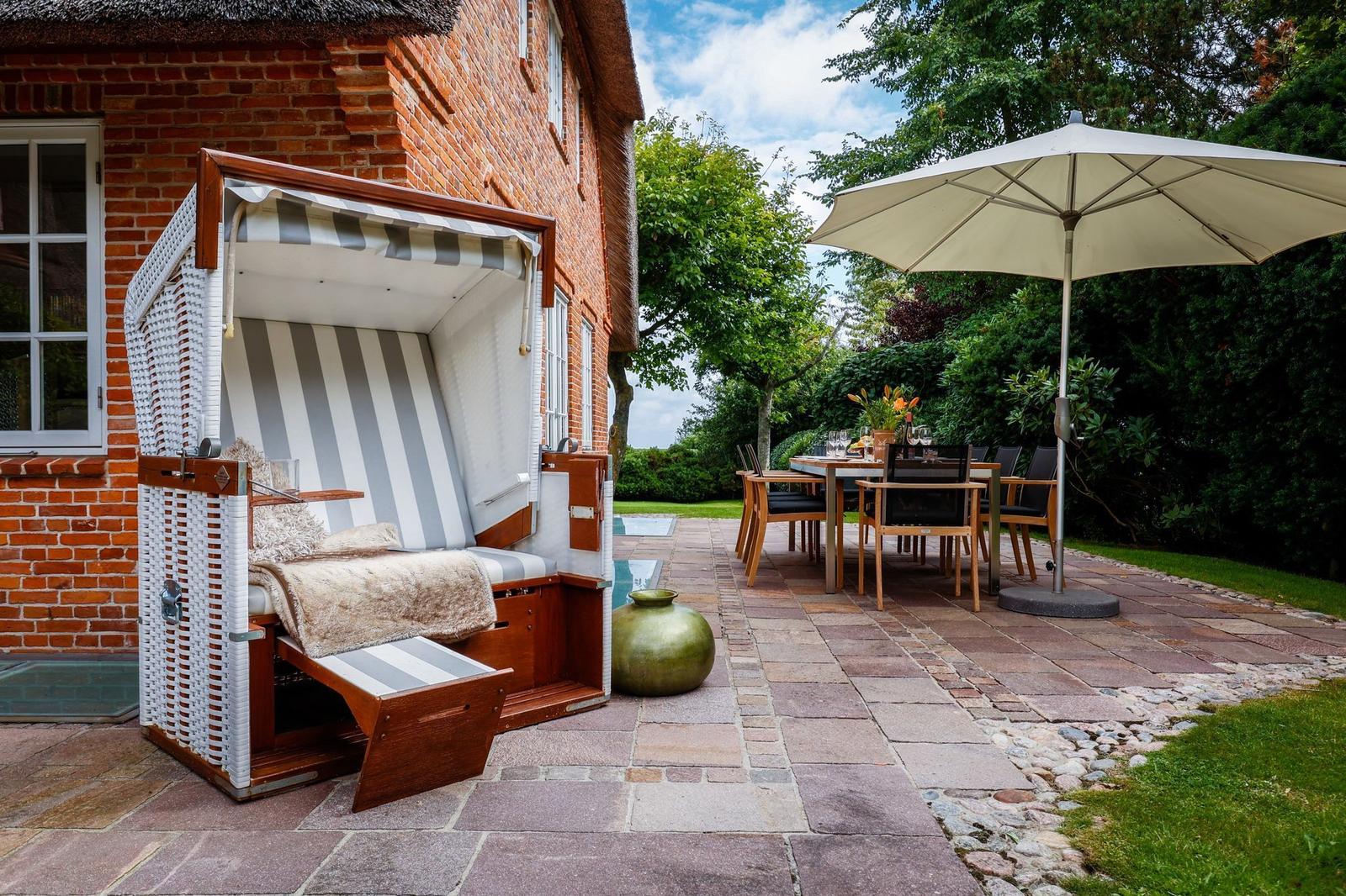 Haus mit Strandkorb und Terrasse mit Tisch, Stühlen und Sonnenschirm.
