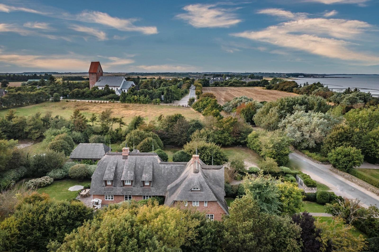 Dorfhaus mit Strohdach, umgeben von Grünflächen und einem See.