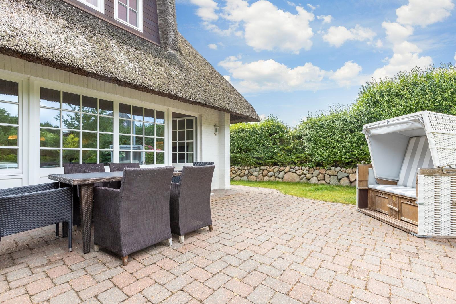 Terrasse mit Sitzgruppe und Strandkorb vor einem Haus mit Strohdach.