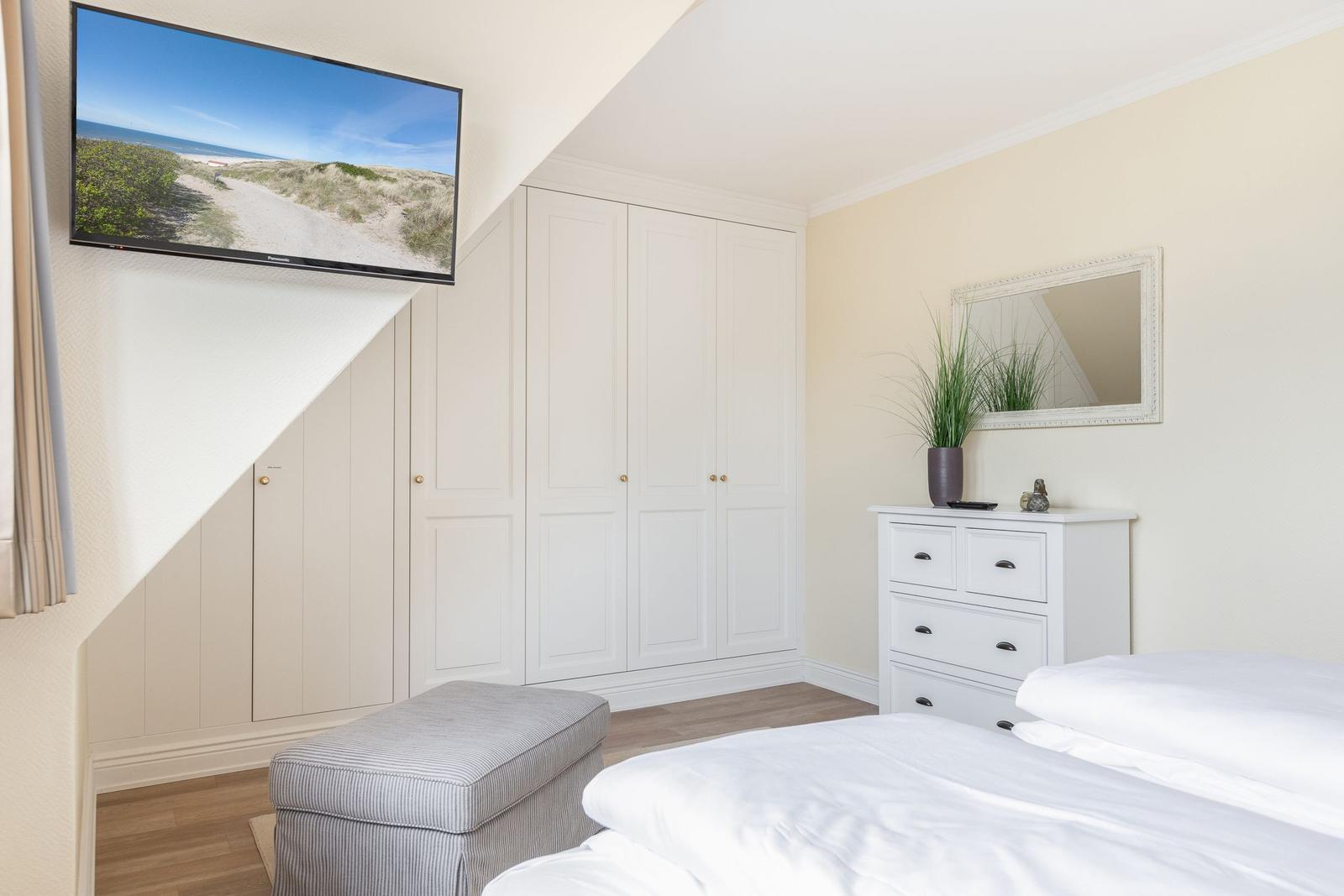 Schlafzimmer mit Bett, Kleiderschrank und Fernseher an der Wand.