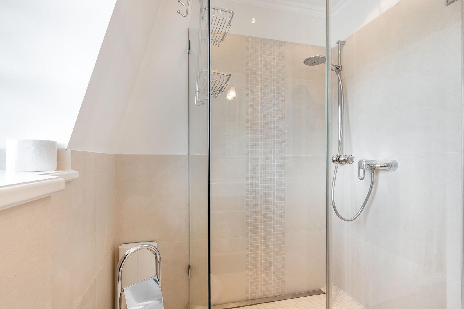 Dusche mit Glaswand, Duschbrause und Mosaikfliesen an der Wand.
