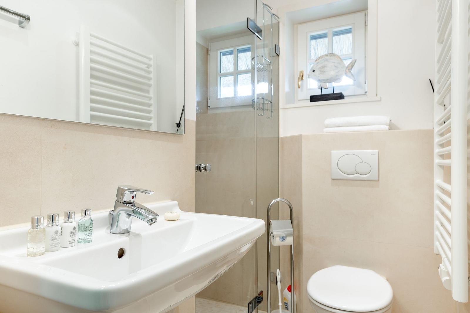 Badezimmer mit Waschbecken, Dusche und Toilette. Fenster mit Fischdekoration.