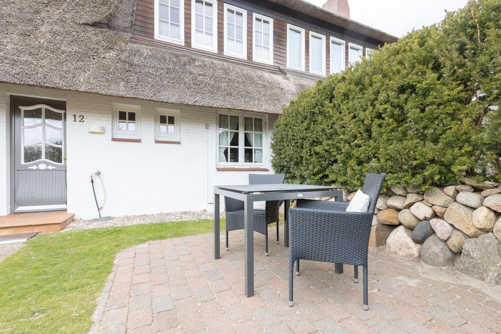 Haus mit strohgedecktem Dach und Außenbereich mit Tisch und Stühlen.