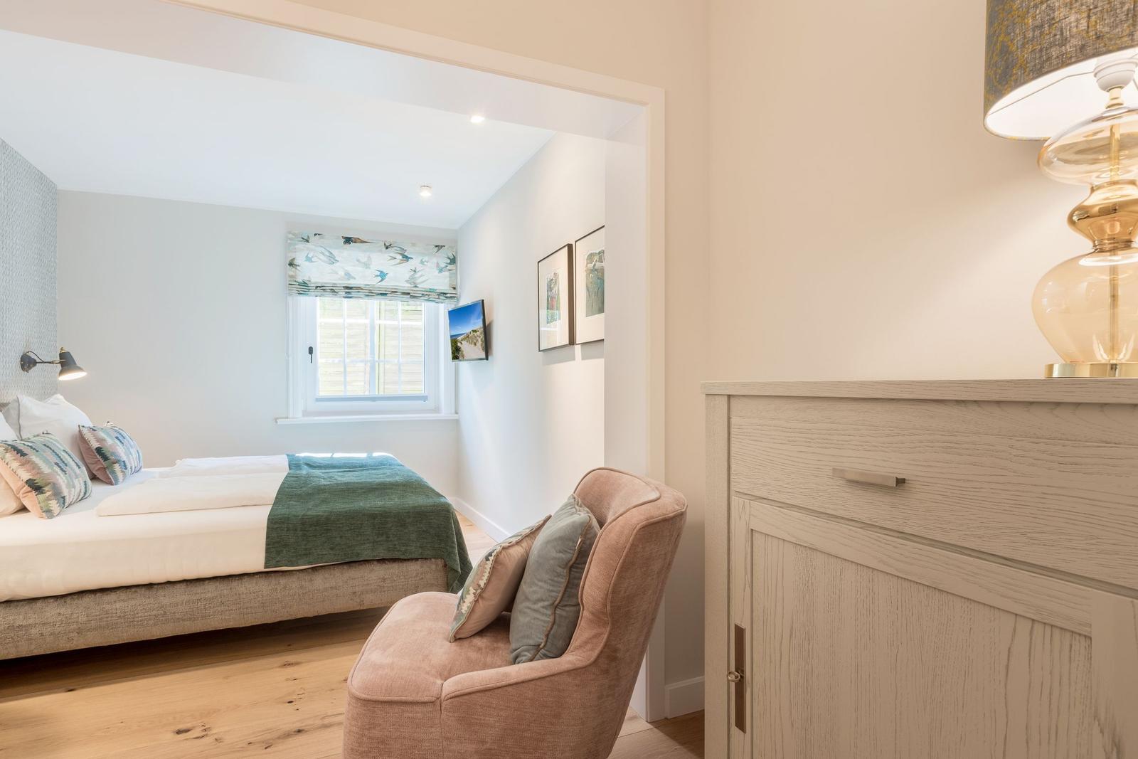 Schlafzimmer mit Bett, Sessel und Schrank. Fenster mit Rollladen und Wandbilder.