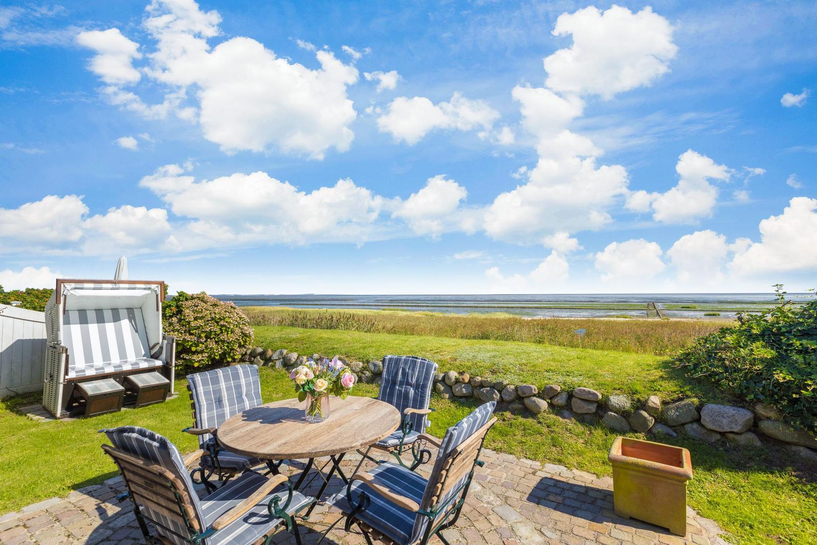 Terrasse mit Tisch und Stühlen, Strandhütte und Blick aufs Meer.
