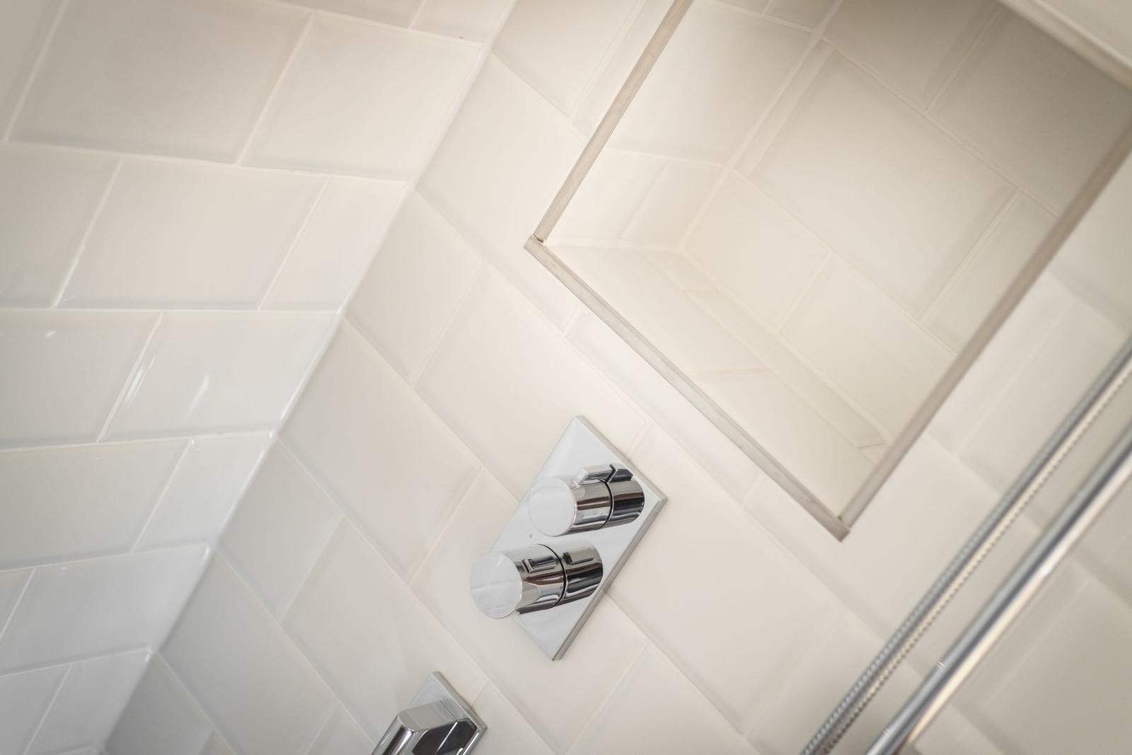 Dusche mit Chromarmaturen und weißen Fliesen