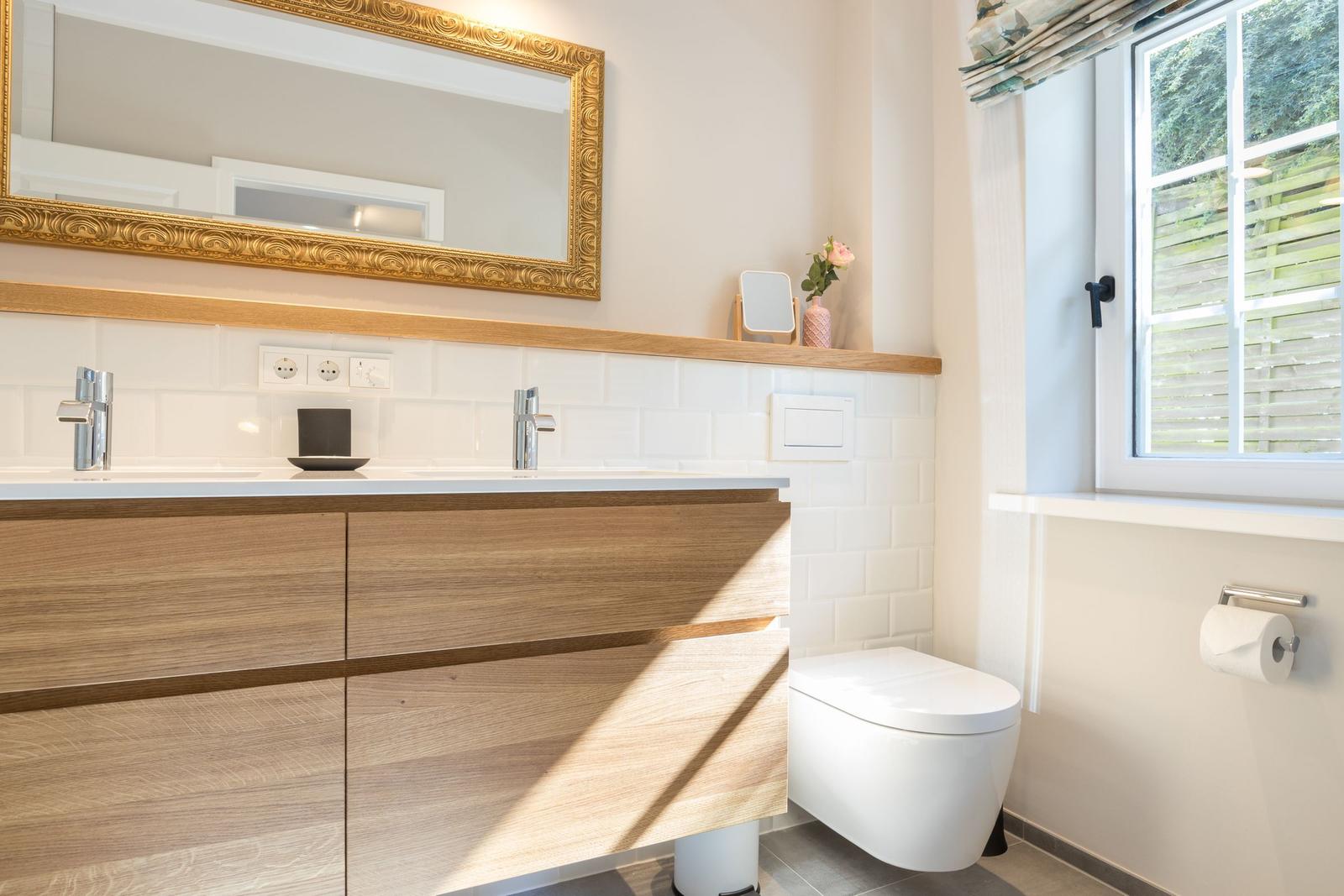 Badezimmer mit Waschtisch, Spiegel und Toilette. Fenster mit Blick auf Garten.