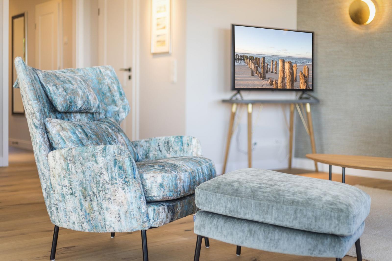 Ein Sessel mit blauem Muster und ein Hocker stehen vor einem Fernseher.