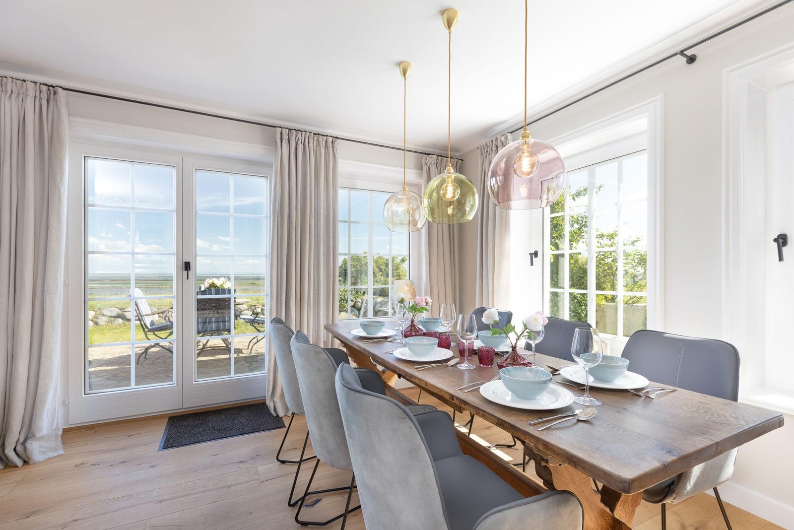 Esszimmer mit Holztisch, grauen Stühlen und großen Fenstern zur Außenterrasse.