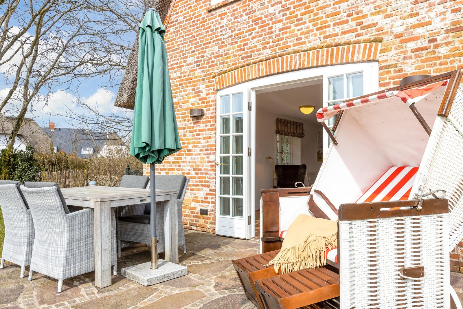 Terrasse mit Esstisch, Stühlen und Strandkorb vor Backsteinhaus