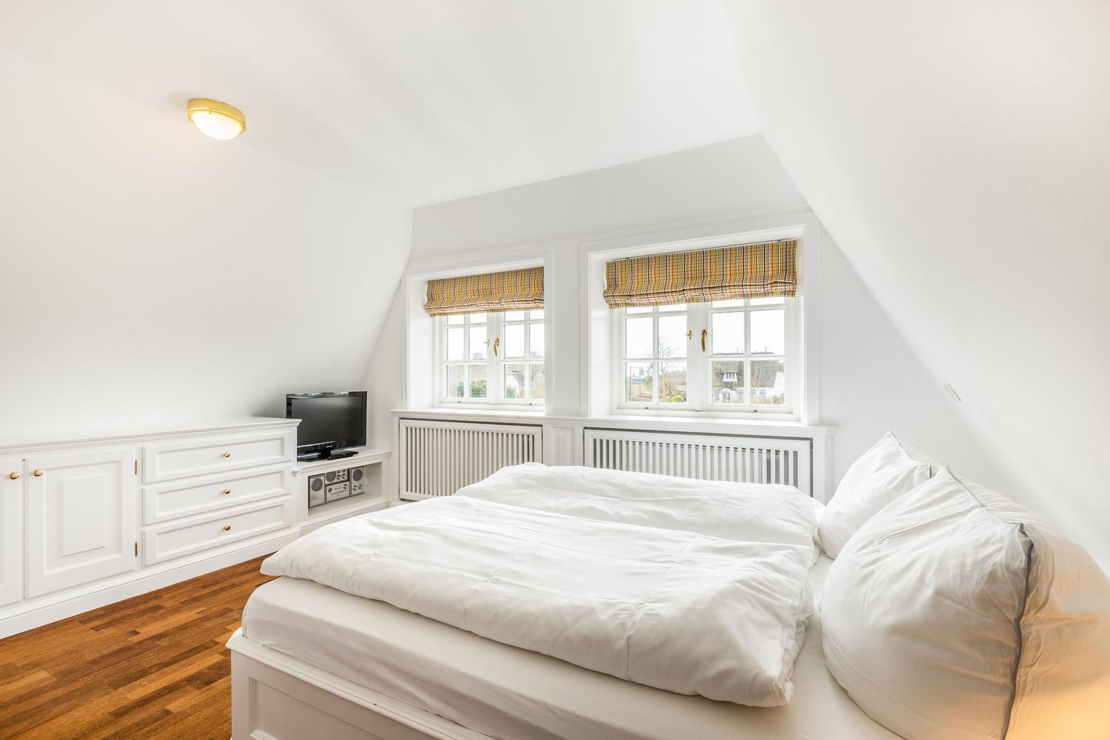 Schlafzimmer mit Doppelbett, zwei Fenstern und Holzboden.
