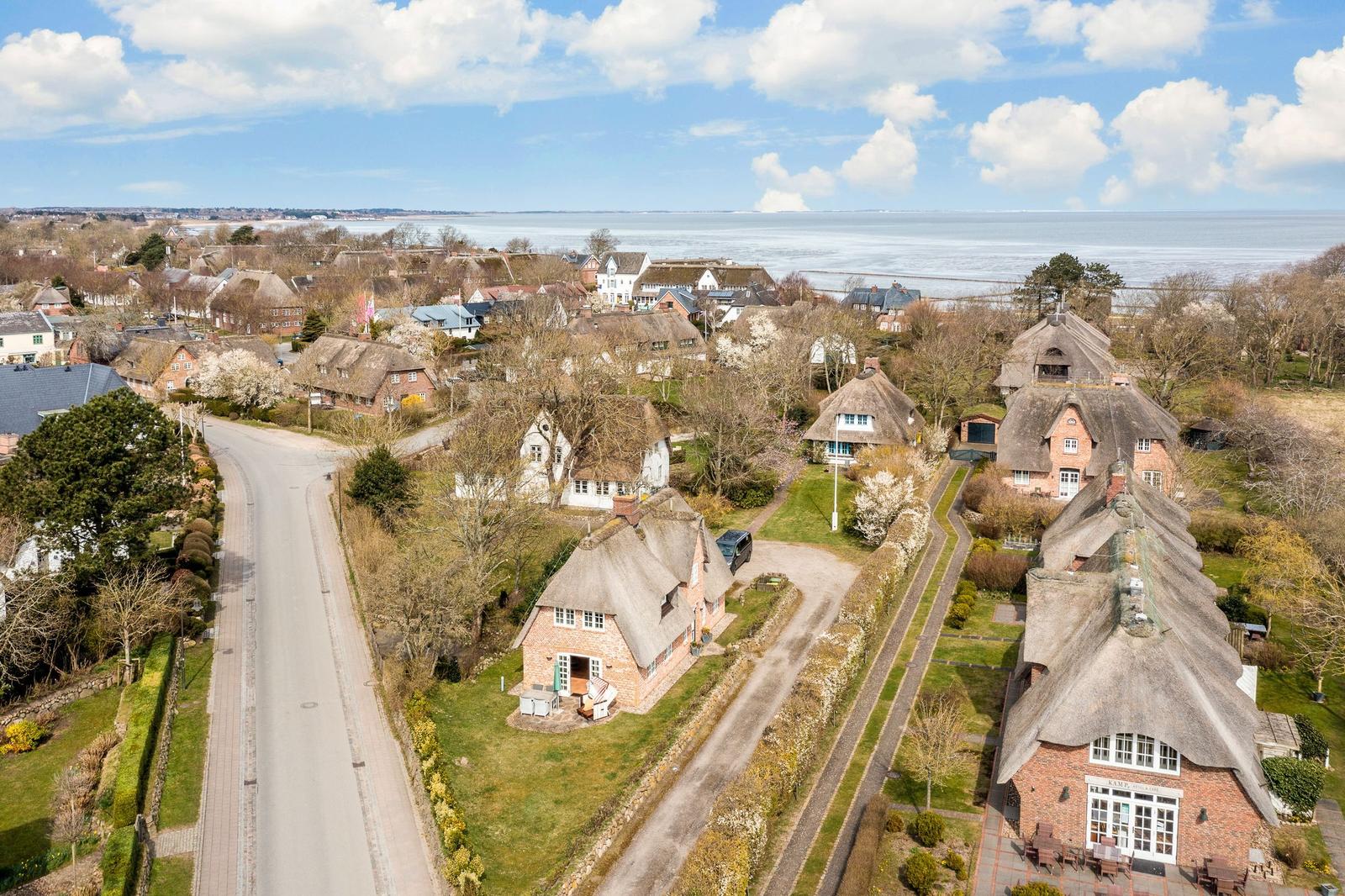 Dorf mit Strohdächern, Straße und Blick aufs Wasser.