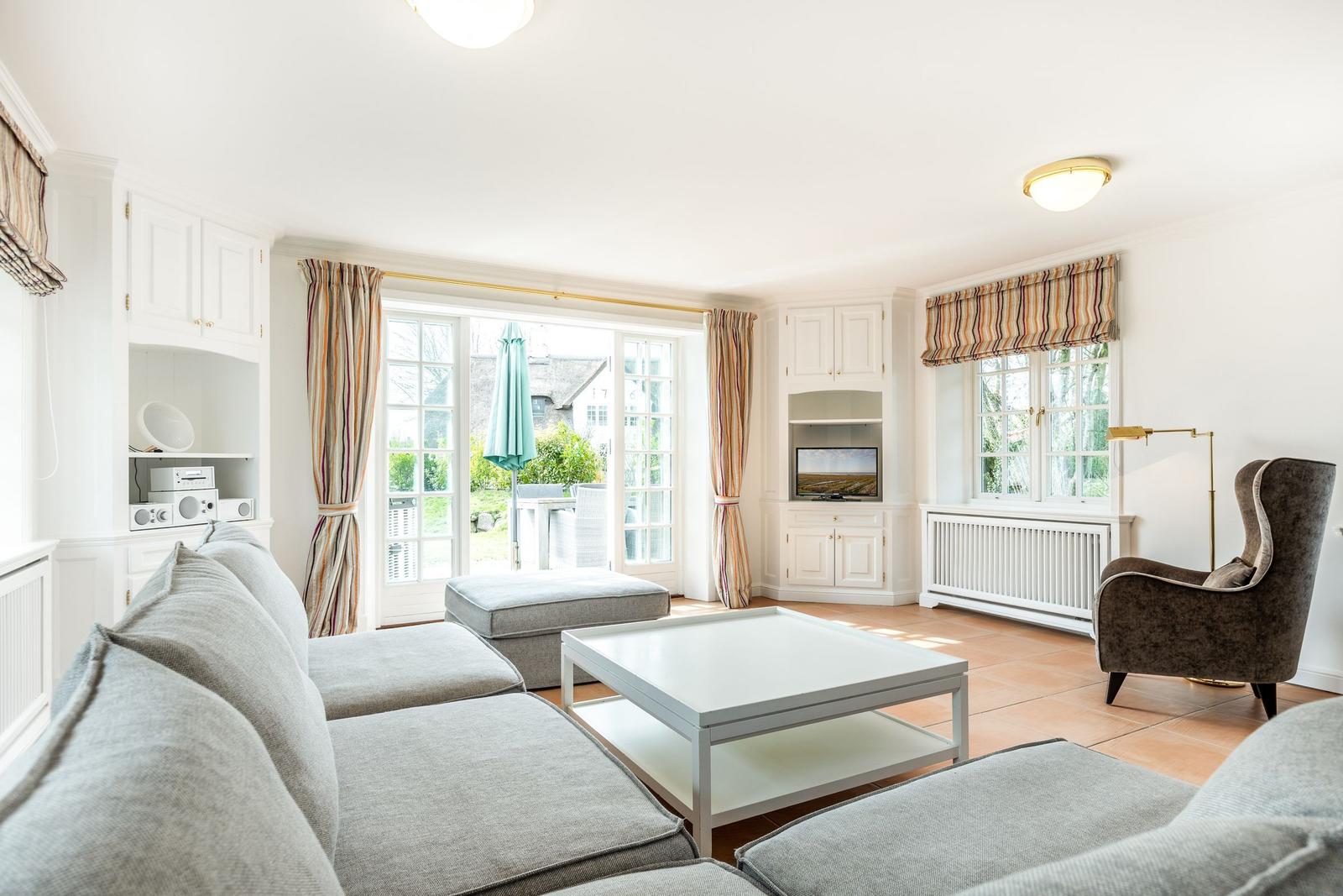 Wohnzimmer mit Sofa, Couchtisch und Fernseher. Durchgangstür zum Garten.