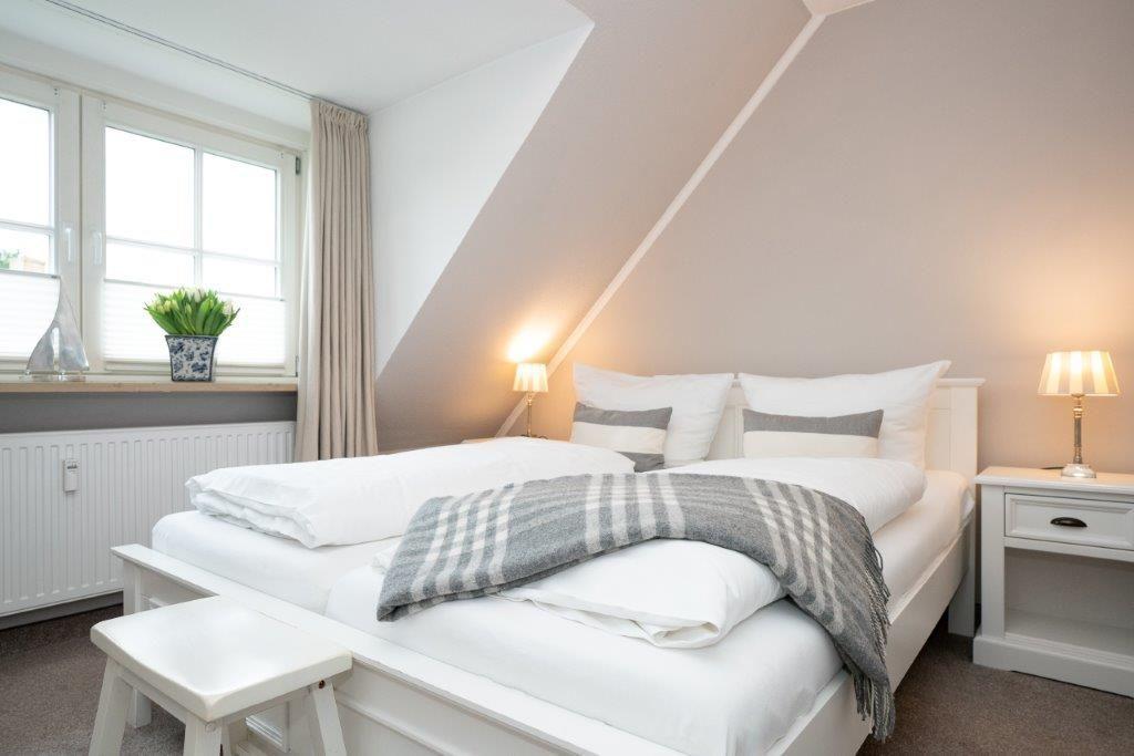 Schlafzimmer mit Dachschrägen, weißem Bett und Nachttisch mit Lampe.