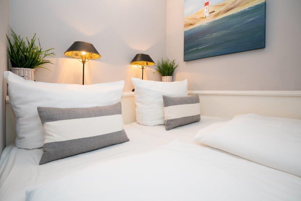 Doppelbett mit weißen Bettwäsche und Kissen, Wandbild und Nachttische mit Lampen.