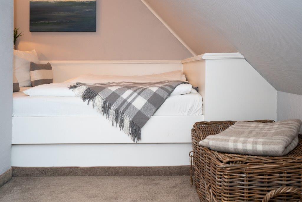 Schlafzimmer mit Dachschräge, weißem Bett und Korb mit Decke.