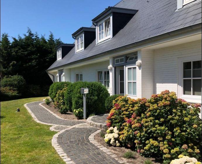 Haus mit Dachgauben, gepflastertem Weg und Blumenbeeten im Vorgarten.
