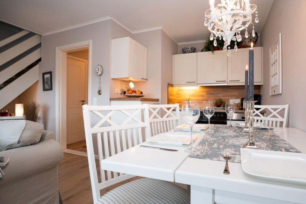 Esszimmer mit weißem Tisch, Stühlen und Kronleuchter. Küche im Hintergrund.