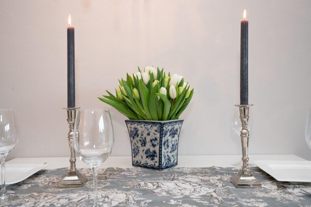 Tisch mit Blumen, Kerzen und Gläsern. Blumenvase mit blau-weißem Muster.