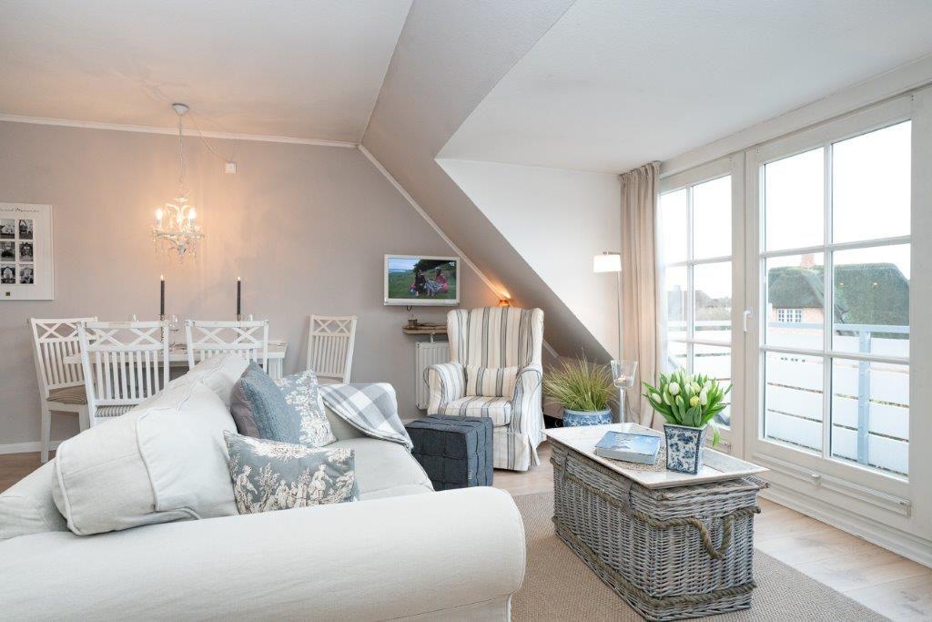 Wohnzimmer mit Sofa, Sessel und Essbereich unter Dachschräge mit Fensterblick.