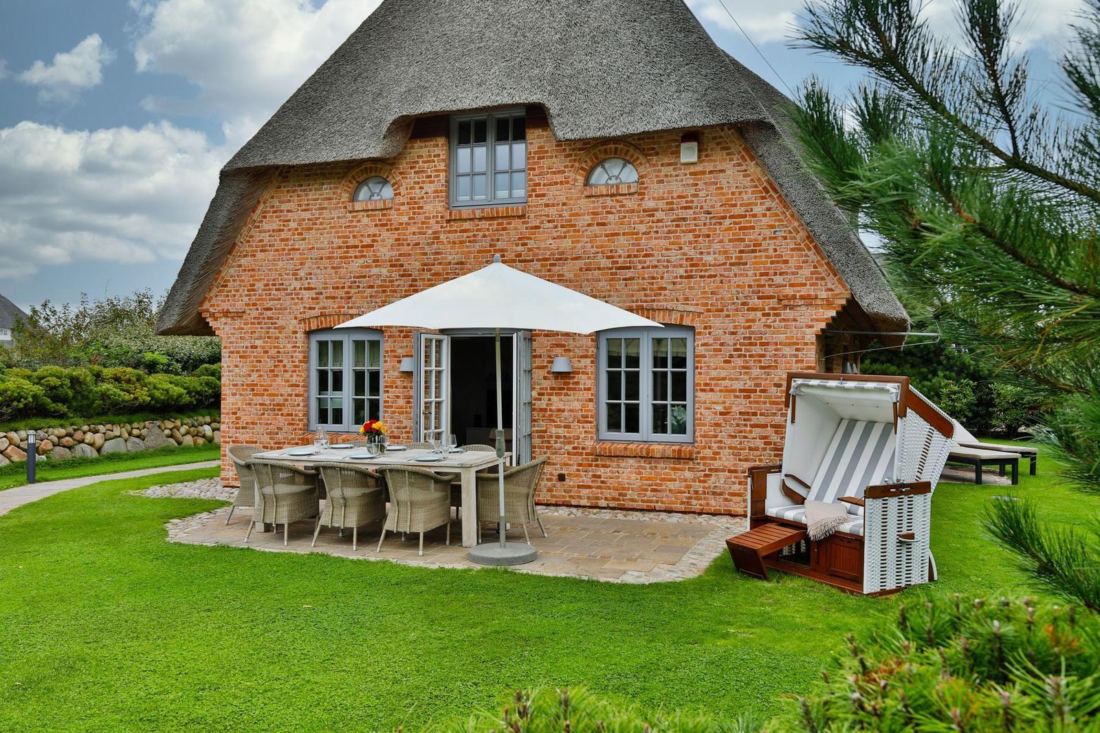 Rotes Backsteinhaus mit Strohdach, Garten mit Tisch, Stühlen und Strandkorb.