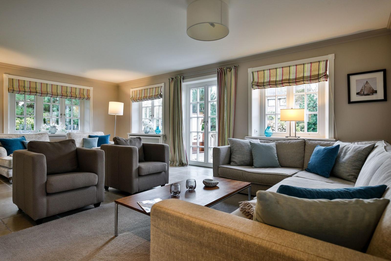 Wohnzimmer mit Sofa, Sesseln und Fenstern mit Gardinen.