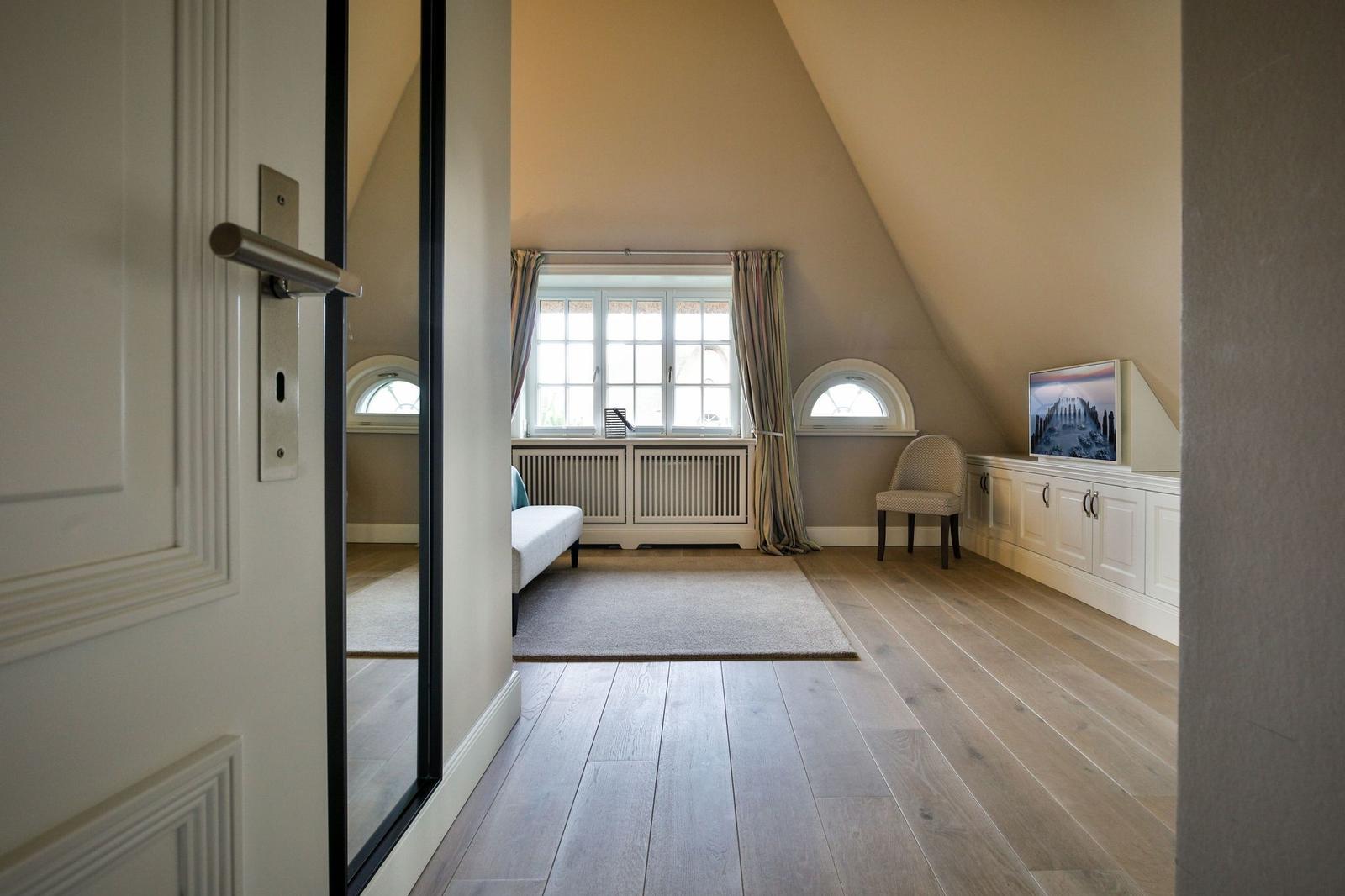 Dachgeschosszimmer mit Holzboden, Fenster und Sitzgelegenheit.