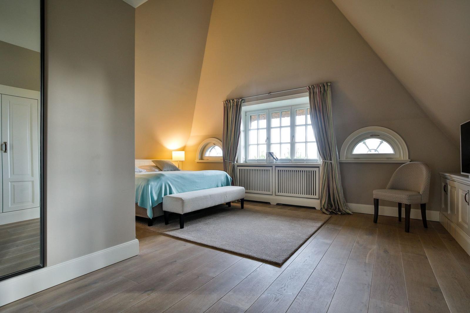 Schlafzimmer mit Dachschräge, Bett, Fenster und Sessel.